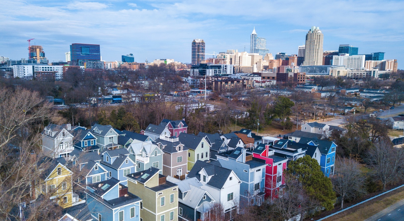 Aerial view of colorful rowhouses with the downtown Raleigh skyline behind